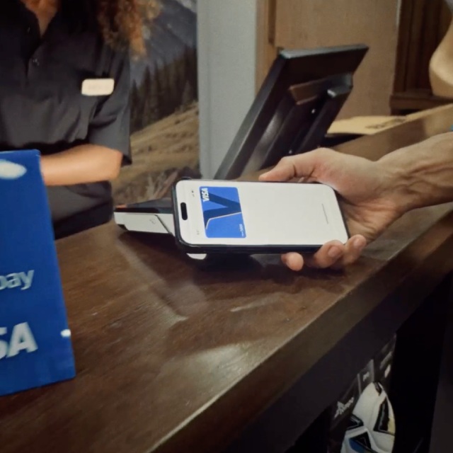 Customer holding a smartphone with a digital card near a payment terminal at a checkout counter