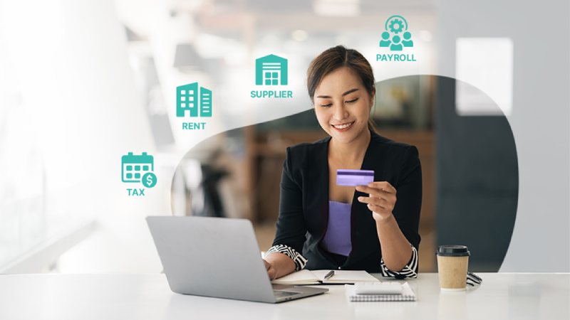 A woman in a black blazer smiles while holding a credit card at a desk with a laptop. Icons labeled Rent, Supplier, Payroll, and Tax surround her.