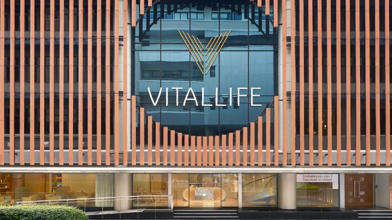 Facade of a modern building with vertical orange panels and a large glass window featuring a stylized "V" logo and the word "Vitallife" in white.