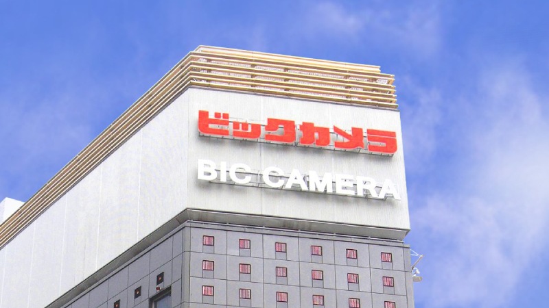 The image shows the top of the Bic Camera building against a blue sky. 