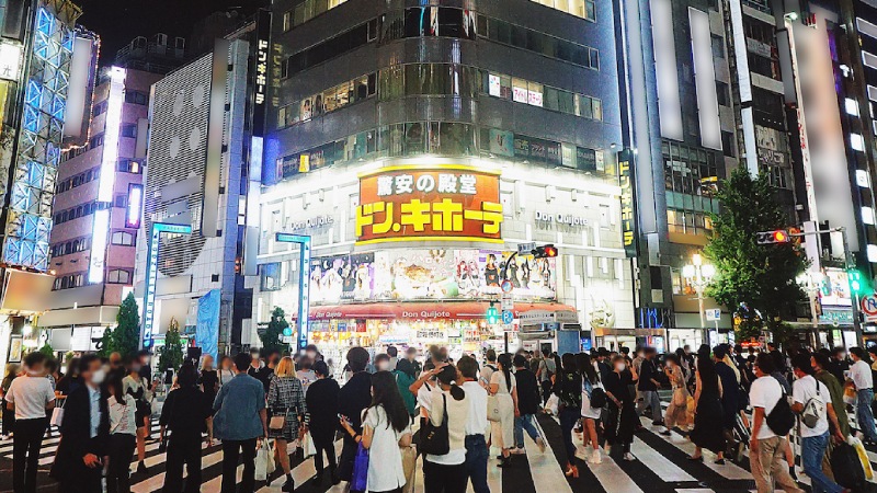 Busy nighttime street scene in Tokyo with crowds crossing at a pedestrian intersection, vibrant city lights, and Don Quijote store in the background.