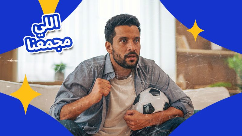 A man intently watches a game on TV, clutching a soccer ball. Arabic text reads "اللي مجمعنا" on a blue and yellow background. 