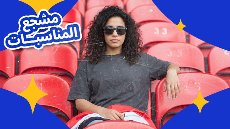 A woman with curly hair and sunglasses sits confidently in red stadium seats, draped in a red, white, and black flag. Arabic text on the left.